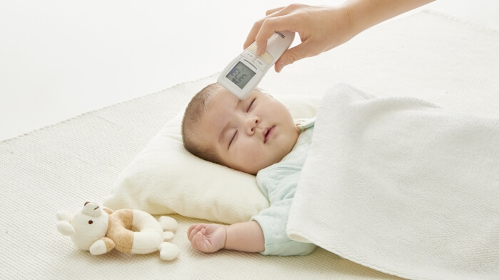 赤ちゃんの額に体温計をかざしている画像